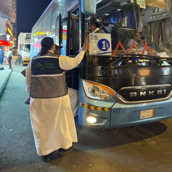 موظف يتابع صعود الحجاج إلى حافلة مسار جدة ومكة ليلاً